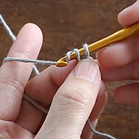 スレッドコードの編み方［5］ループを指で押さえ、針に糸をかけて2つのループをくぐらせます。